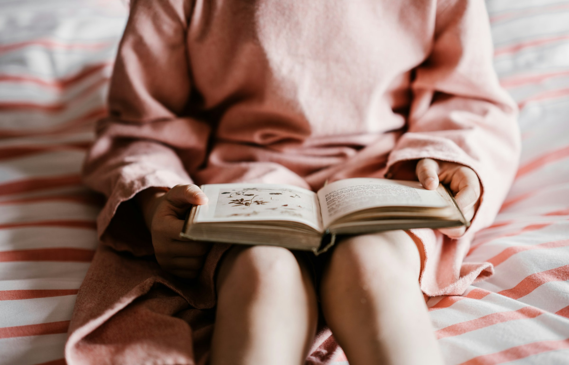 A child seated on a bed reading a small book