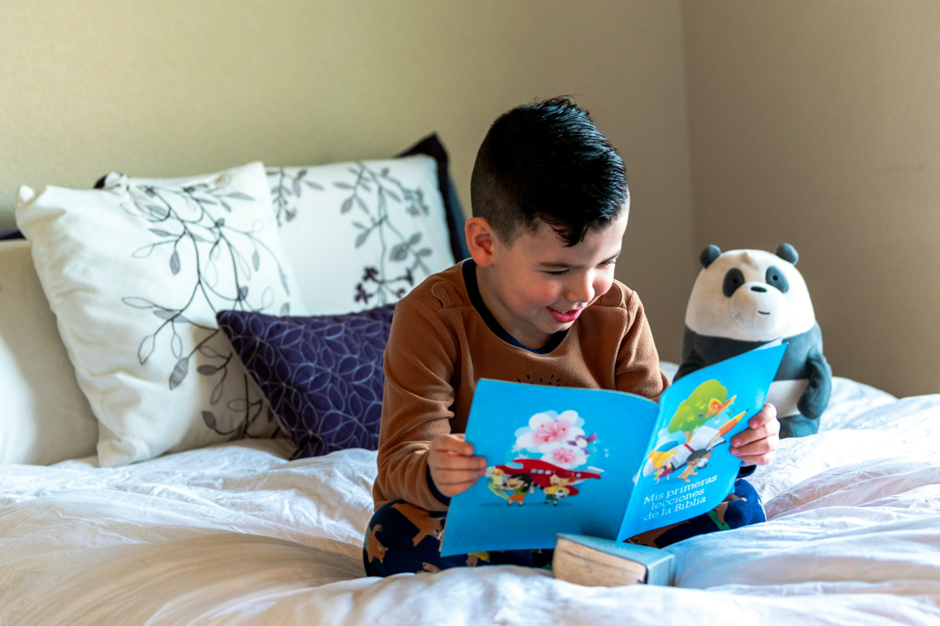 A smiling child reading a colorful book on a bed