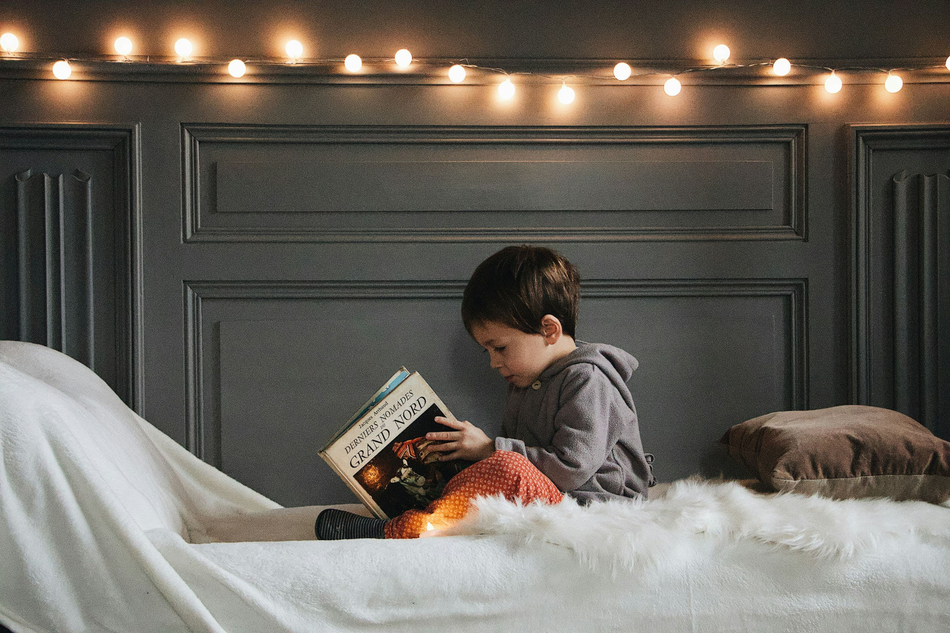 A young child reading beneath warm string lights